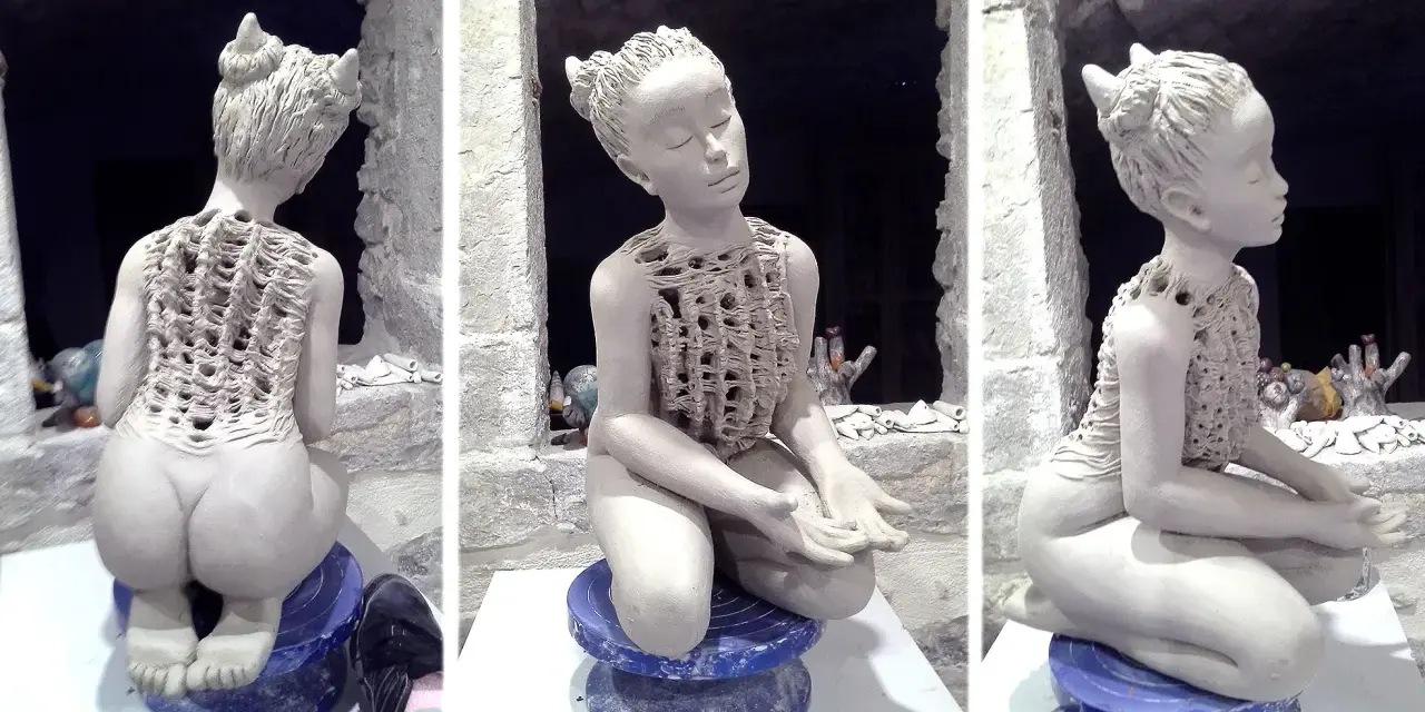 Sculpture en argile d'une jeune fille aux cornes, assise, vêtue d'une tunique ajourée.