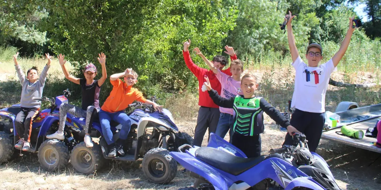 Des enfants joyeux sur des quads, bras levés, en extérieur.