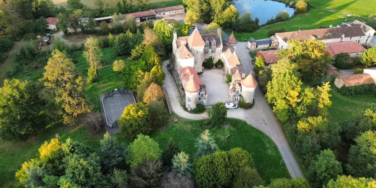 Vue aérienne d'un château entouré d'arbres, avec un étang et un terrain de sport.