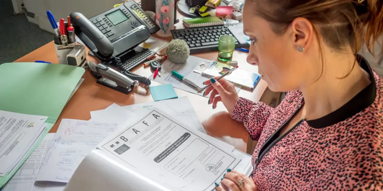 Une femme examine un document BAFA sur un bureau encombré.