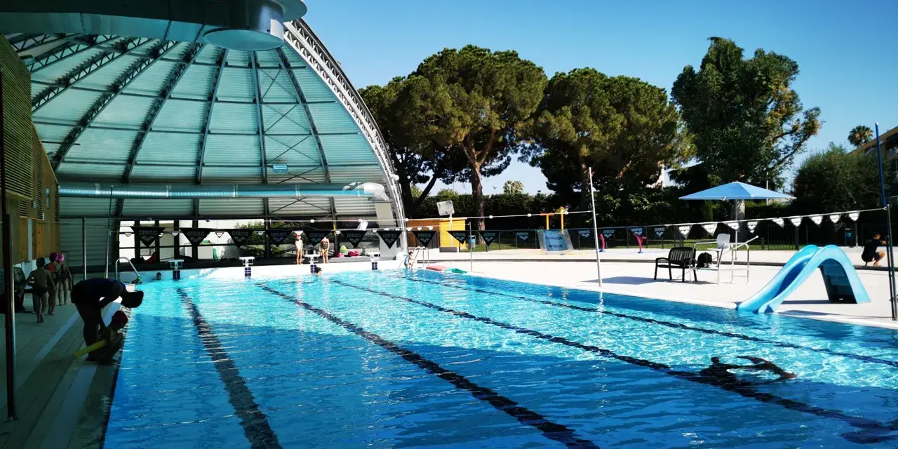 Piscine intérieure avec toboggan bleu, lignes de nage et quelques personnes.