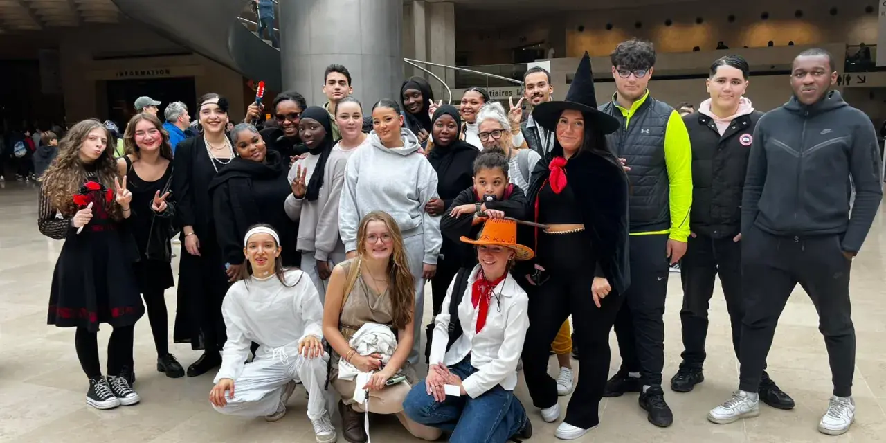 Un groupe de jeunes gens, certains déguisés, pose pour une photo dans un hall moderne.