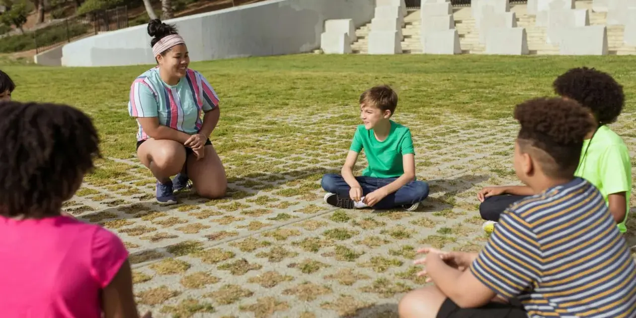 Une animatrice discute avec des enfants assis en cercle dans un parc.
