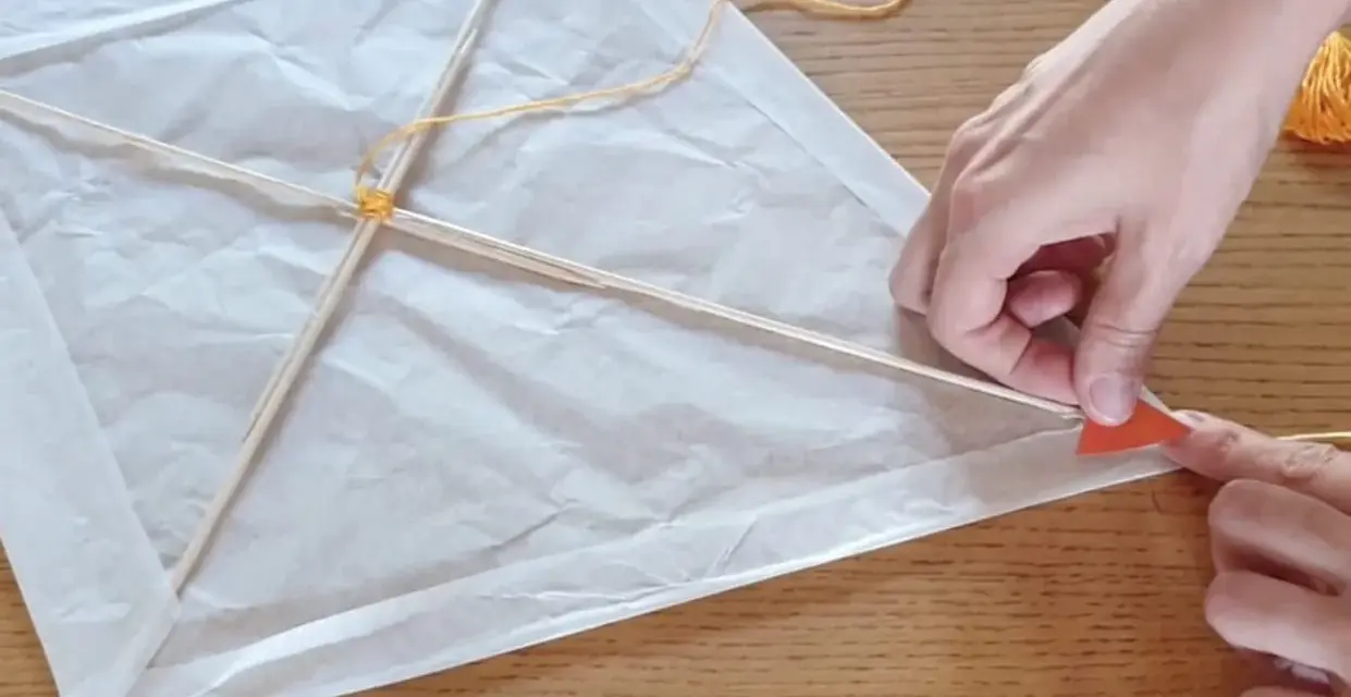 Mains fabriquant un cerf-volant en papier blanc avec des bâtons de bois et de la ficelle.