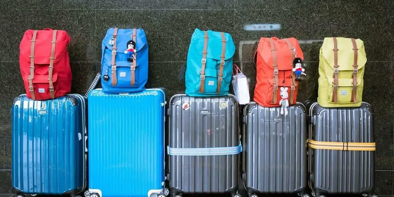 Six valises de différentes couleurs empilées, avec des sacs à dos colorés sur le dessus.