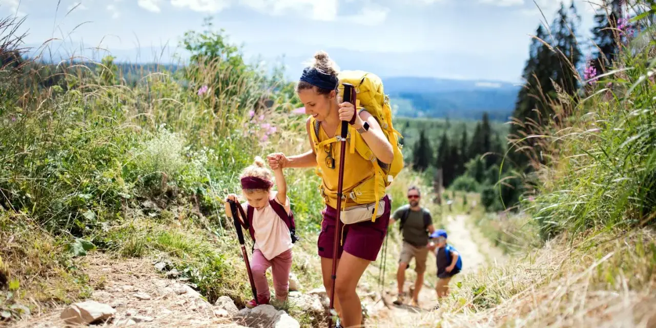 Famille faisant de la randonnée en montagne, une mère aide sa fille à monter un sentier.