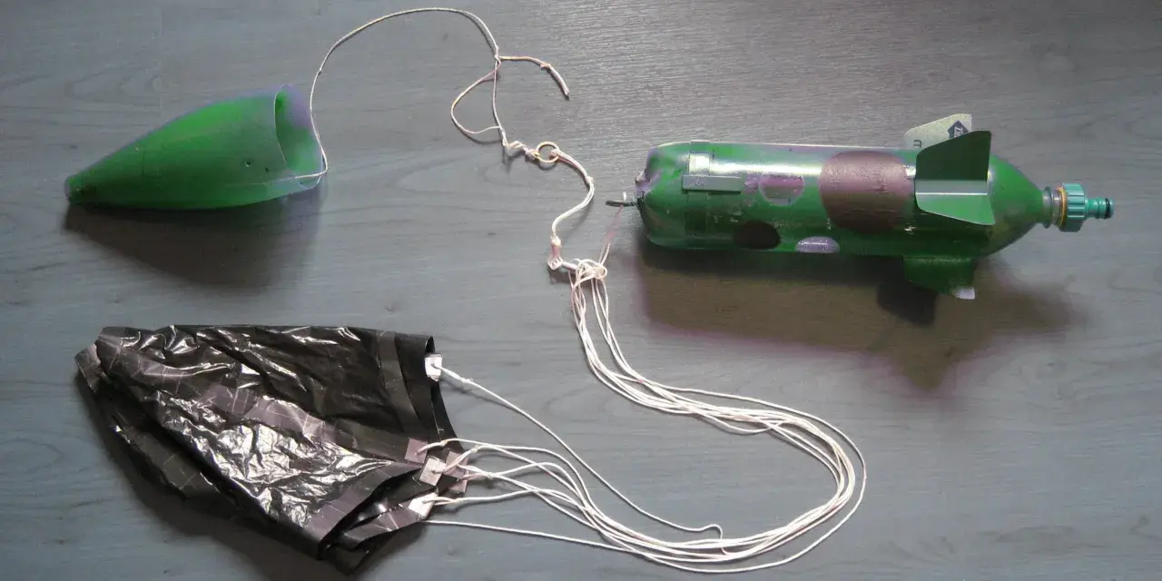 Fusée à eau verte avec cône, parachute noir et fils blancs sur fond gris.