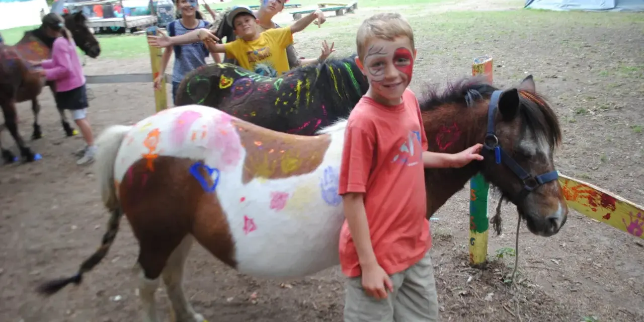Enfants avec des poneys décorés de peinture, dans un campement avec des tentes.