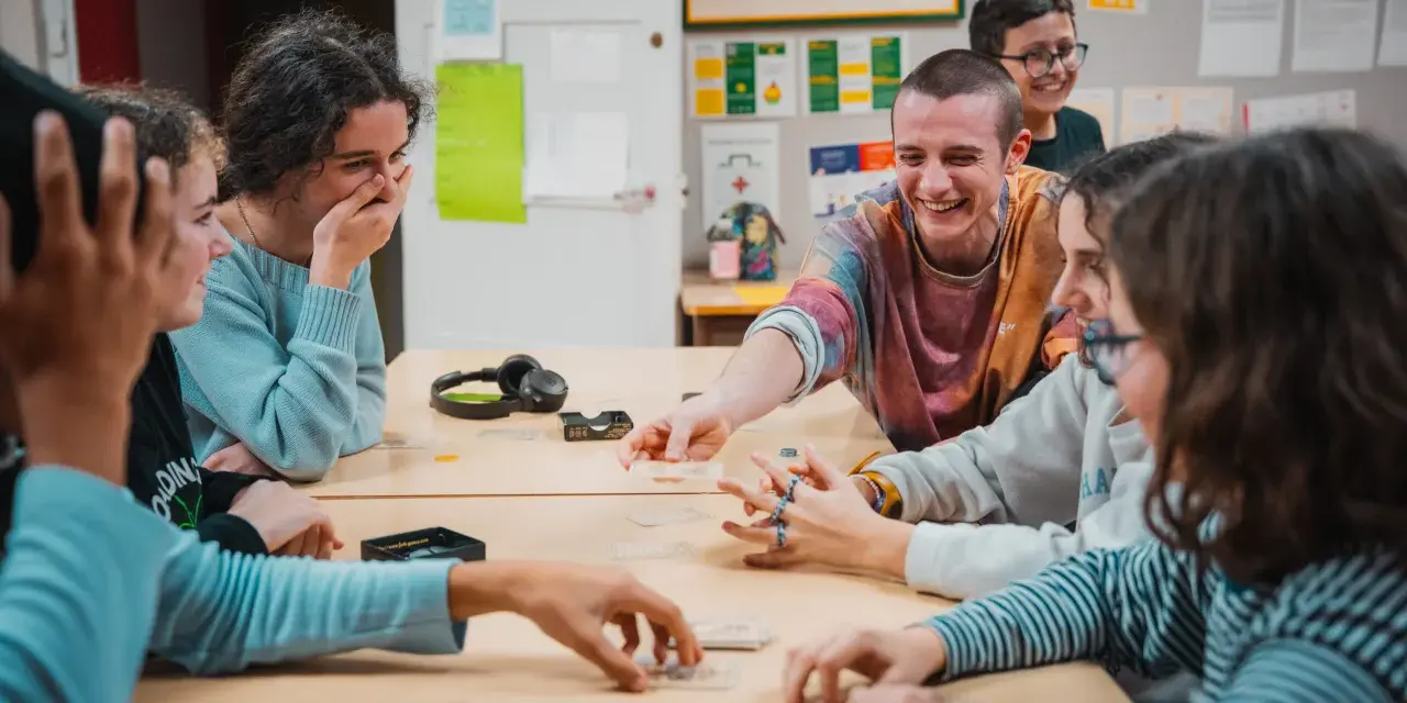 Des jeunes rient en jouant à un jeu de cartes autour d'une table.