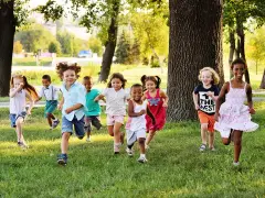 Des enfants joyeux courent dans l'herbe, profitant d'une journée ensoleillée dans une colonie de vacances 3-6 ans.