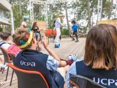 Des jeunes participent à des stages BAFA, observant une scène en plein air. L'un porte une couronne en carton.