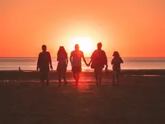Une famille profite de ses vacances à l'étranger, marchant main dans la main sur une plage au coucher du soleil.