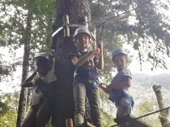 Trois enfants casqués s'amusent sur un parcours accrobranche, une activité typique d'une colonie de vacances en Savoie.