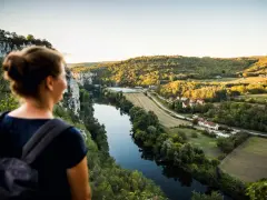 Une femme admire un paysage de carte postale lors de son voyage découverte en France. La rivière serpente à travers des collines verdoyantes et des villages pittoresques.