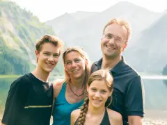 Famille souriante au bord d'un lac, paysage montagneux. Une belle idée pour savoir comment partir en famille d'accueil.