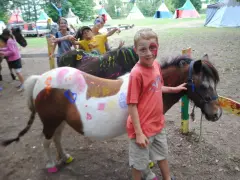 Enfants joyeux avec des poneys décorés, visages peints, dans un campement de vacances Far West.