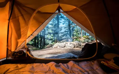 Vue de l'intérieur d'une tente orange, un feu crépite dehors. L'obligation sécurité camping est respectée avec ce campement bien installé.