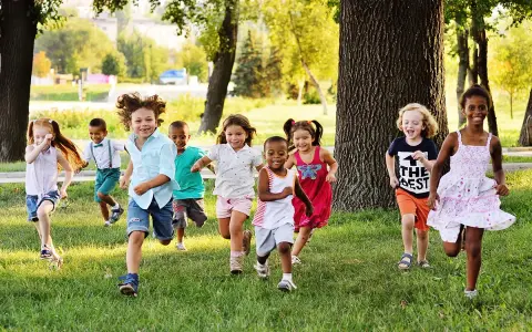 Des enfants joyeux courent dans l'herbe, profitant d'une journée ensoleillée dans une colonie de vacances 3-6 ans.