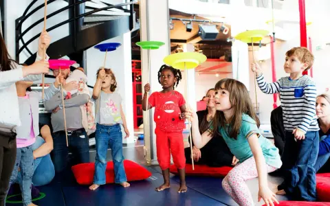 Des enfants apprennent à faire tourner des assiettes sur des bâtons lors d'un atelier cirque.