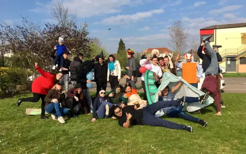 Groupe de jeunes en costumes et déguisements, certains sur une tente, sur l'herbe par beau temps.