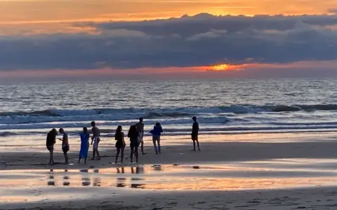 Coucher de soleil sur une plage avec des silhouettes de personnes.