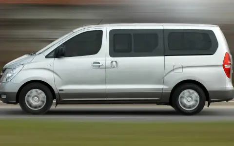 Un mini bus argenté roule sur une route. Ce véhicule spacieux est idéal pour les familles ou les groupes, et peut être conduit avec un permis B.