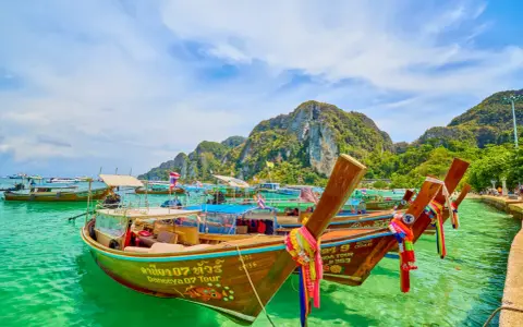 Bateaux traditionnels thaïlandais amarrés dans une eau turquoise, avec des montagnes verdoyantes en arrière-plan.
