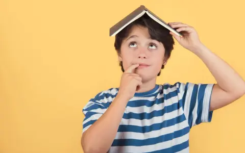 Un enfant de 5 ans, avec un livre sur la tête, réfléchit. Il est en colonie de vacances.