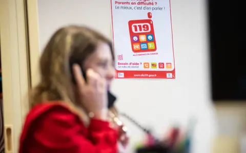 Une femme au téléphone, devant une affiche expliquant le crip signification du numéro 119 pour les enfants en danger.