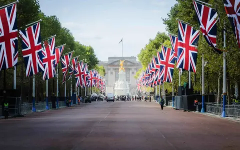 Allée bordée de drapeaux britanniques menant à un palais, avec des arbres et des gardes.