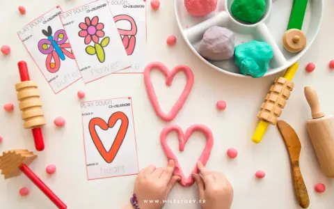Pâte à modeler rose en forme de cœur, cartes d'activités, rouleaux et petites boules de pâte.