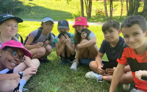 Groupe d'enfants souriants assis dans l'herbe, certains tenant des cartes.