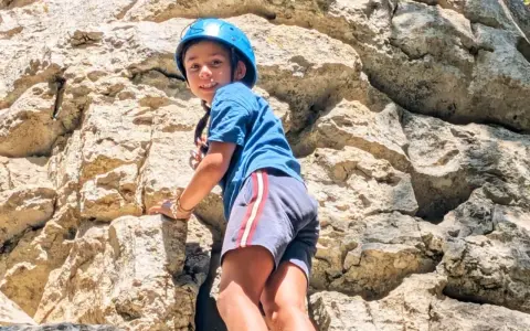 Enfant souriant escaladant un rocher avec un casque bleu.