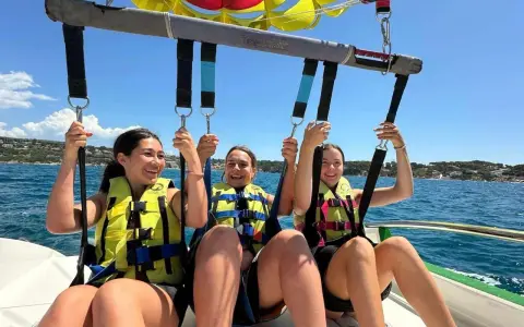 Trois jeunes femmes souriantes en parachute ascensionnel au-dessus de la mer.