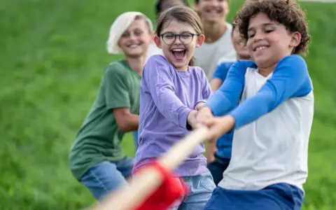 Des enfants joyeux jouent à la corde dans un champ d'herbe verte.
