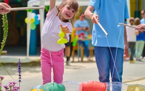 Une petite fille joyeuse participe à des jeux de kermesse pour tout petit, essayant d'attraper un jouet jaune avec une canne à pêche improvisée.