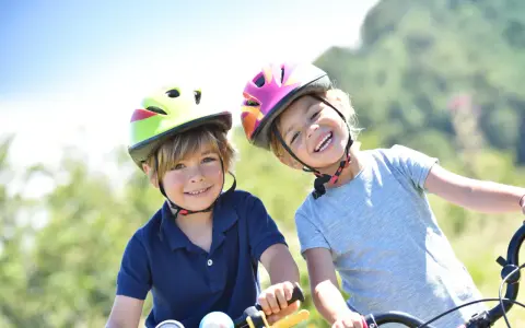 Deux enfants souriants, casques de vélo colorés, profitent de leurs vacances scolaires en Savoie.