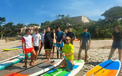 Un groupe d'adolescents et un moniteur sur une plage avec des planches de paddle.