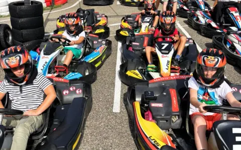 Des enfants casqués prêts pour une course de colo karting, le sourire aux lèvres, impatients de démarrer.