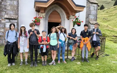 Groupe d'enfants en tenue de randonnée devant une petite église en montagne.