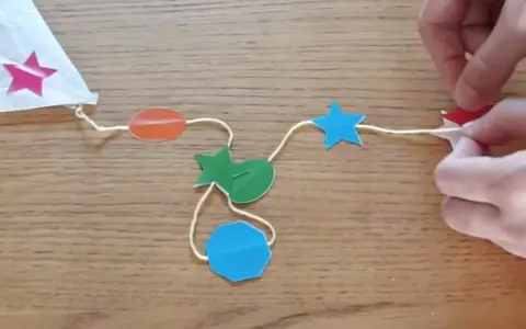 Fabrication d'un cerf-volant étoile : fils, formes colorées (étoiles, ovales, octogone) et mains.