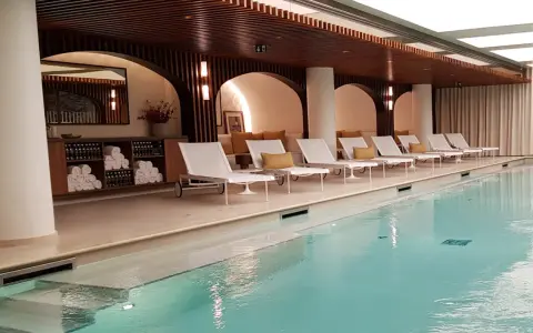 Piscine intérieure avec chaises longues blanches, coussins jaunes et étagères de serviettes.