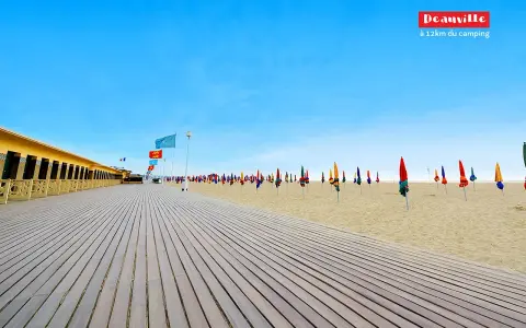 Plage de Deauville, parfaite pour une vacance scolaire en Normandie. Cabines colorées, parasols et ciel bleu azur.
