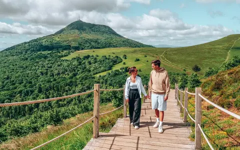 Couple marchant sur un chemin en bois avec un volcan en arrière-plan en Auvergne.