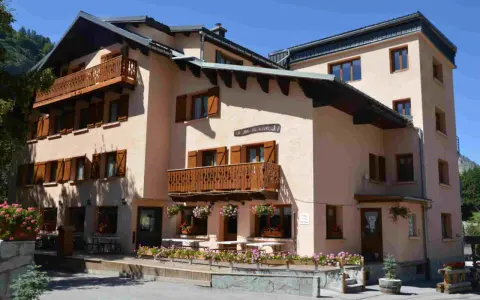 Bâtiment de style alpin avec balcons en bois et volets marrons, fleuri. Une enseigne "La Joie de Vivre" suggère une ambiance de colonie en Haute-Savoie.