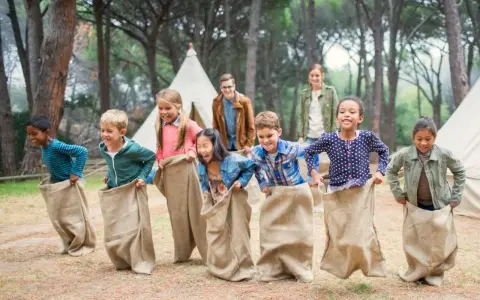 Des enfants participent à une course en sac dans un camp de vacances en forêt.