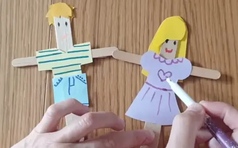 Poupées en bâtonnets de bois, une fille et un garçon, décorées par des mains d'enfant.