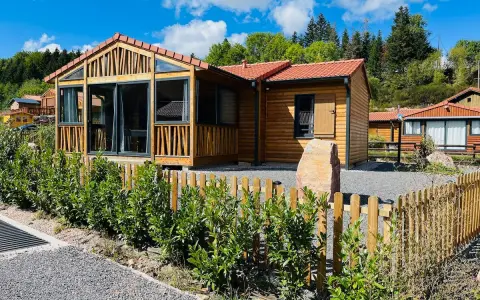 Chalets en bois avec clôture et végétation devant, sous un ciel bleu.