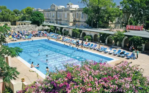 Profitez de vos vacances scolaires à Malte au bord de cette piscine animée, entourée de transats et de végétation luxuriante.