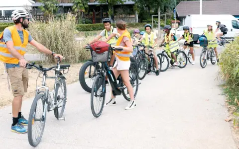 Un groupe d'enfants à vélo, encadrés par des adultes en gilets de sécurité, suit un parcours. La scène illustre la réglementation du déplacement à pied et à vélo à l'ACM.